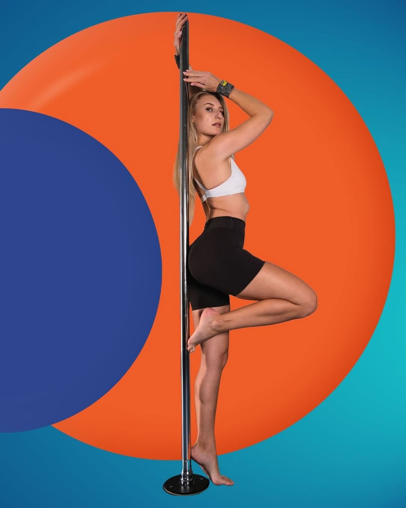 A pole dancer in a white sports top and black shorts posing against the pole in front of bold orange and blue circles, wearing SneakyDeez wrist wraps