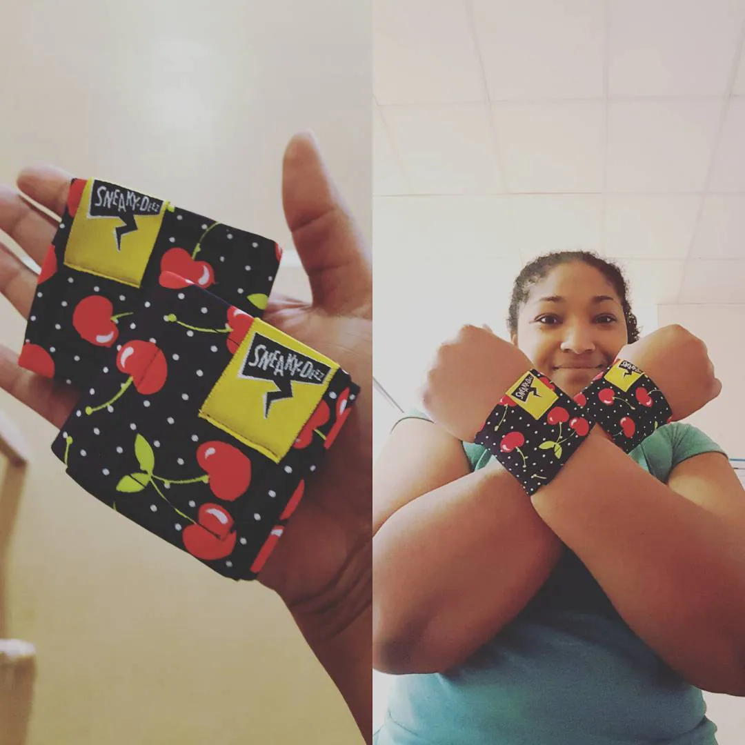 Two photos side by side of a SneakyDeez customer's black cherry-print wrist wraps, one with the pair held up in her hand and one with her smiling and wearing them on both wrists with her arms crossed